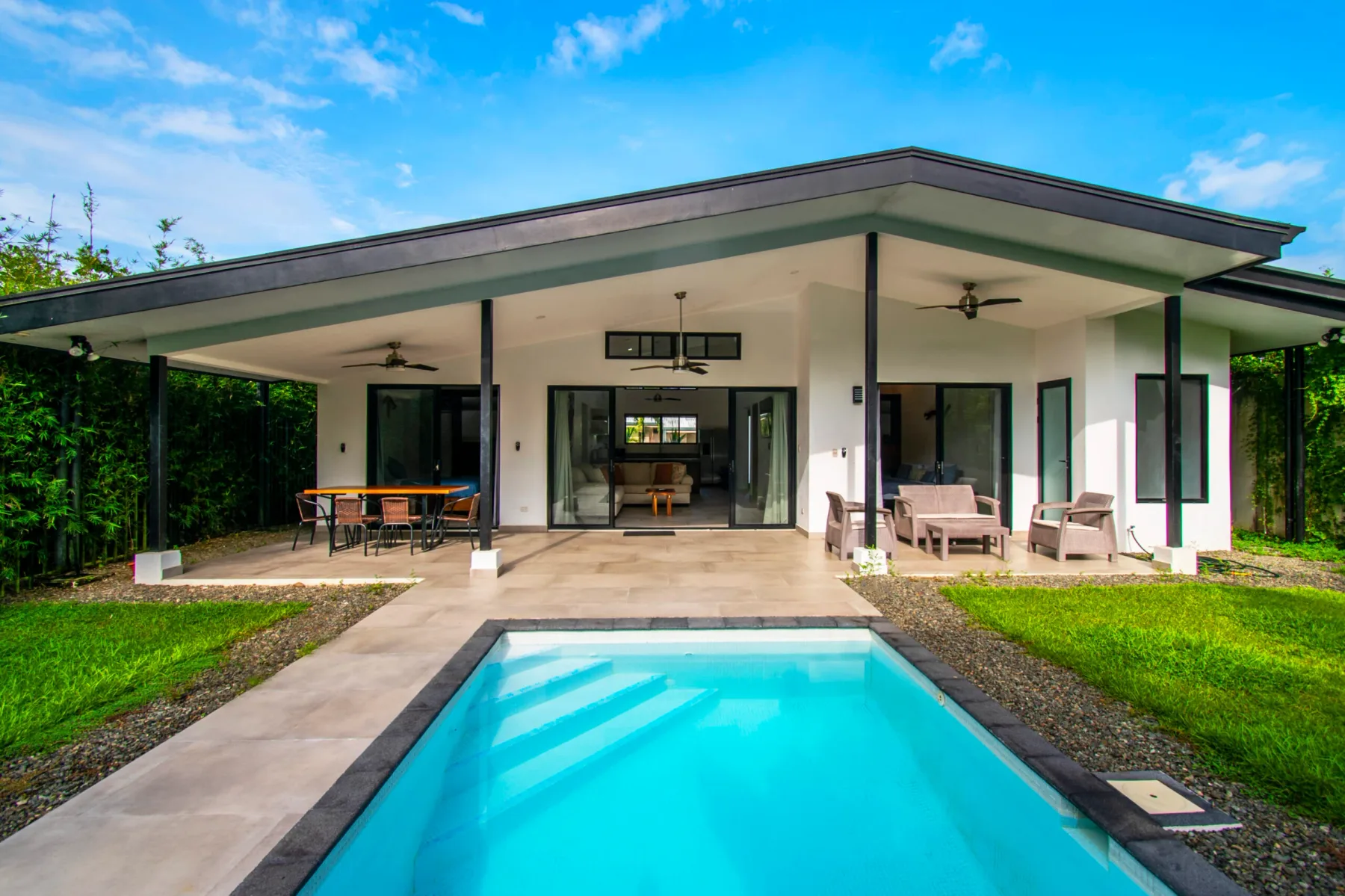 A modern house opens onto a covered patio beside a swimming pool.