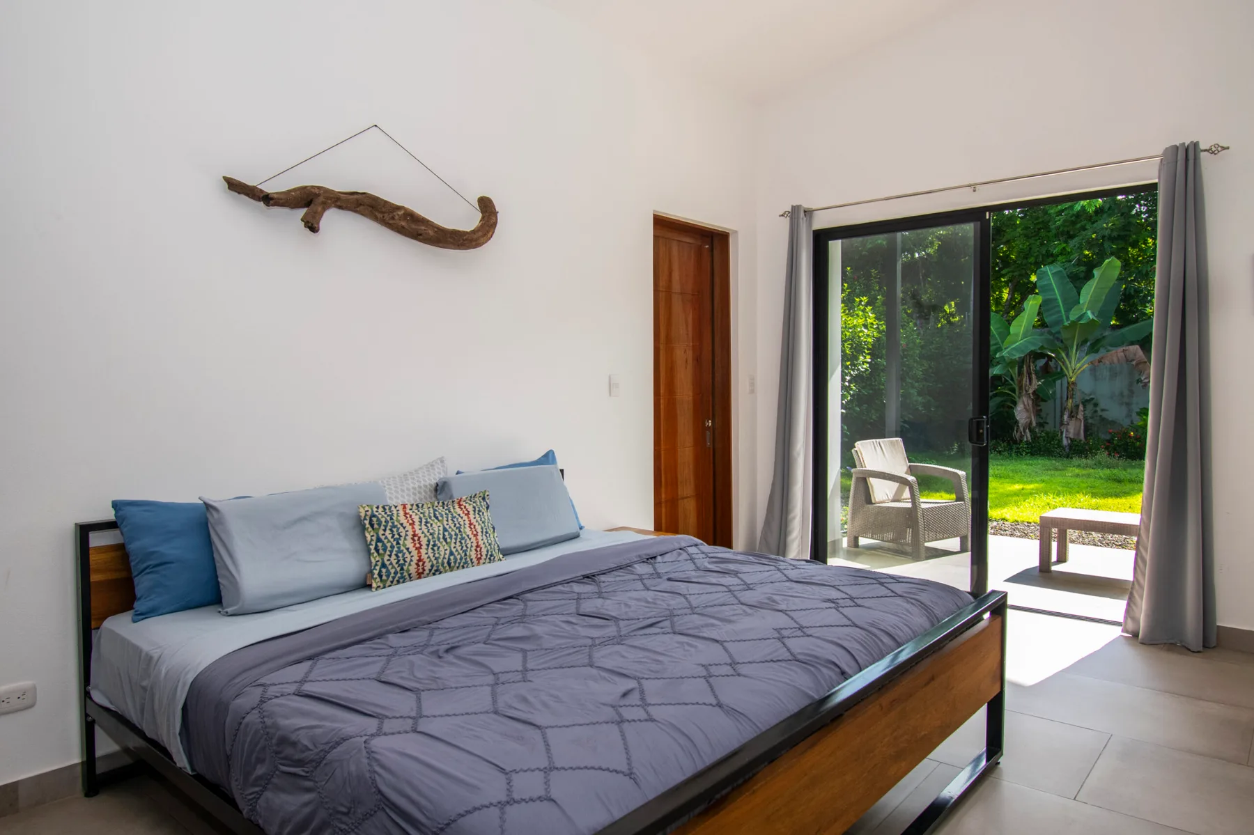 A bedroom with a large bed beside sliding glass doors opening onto a garden.