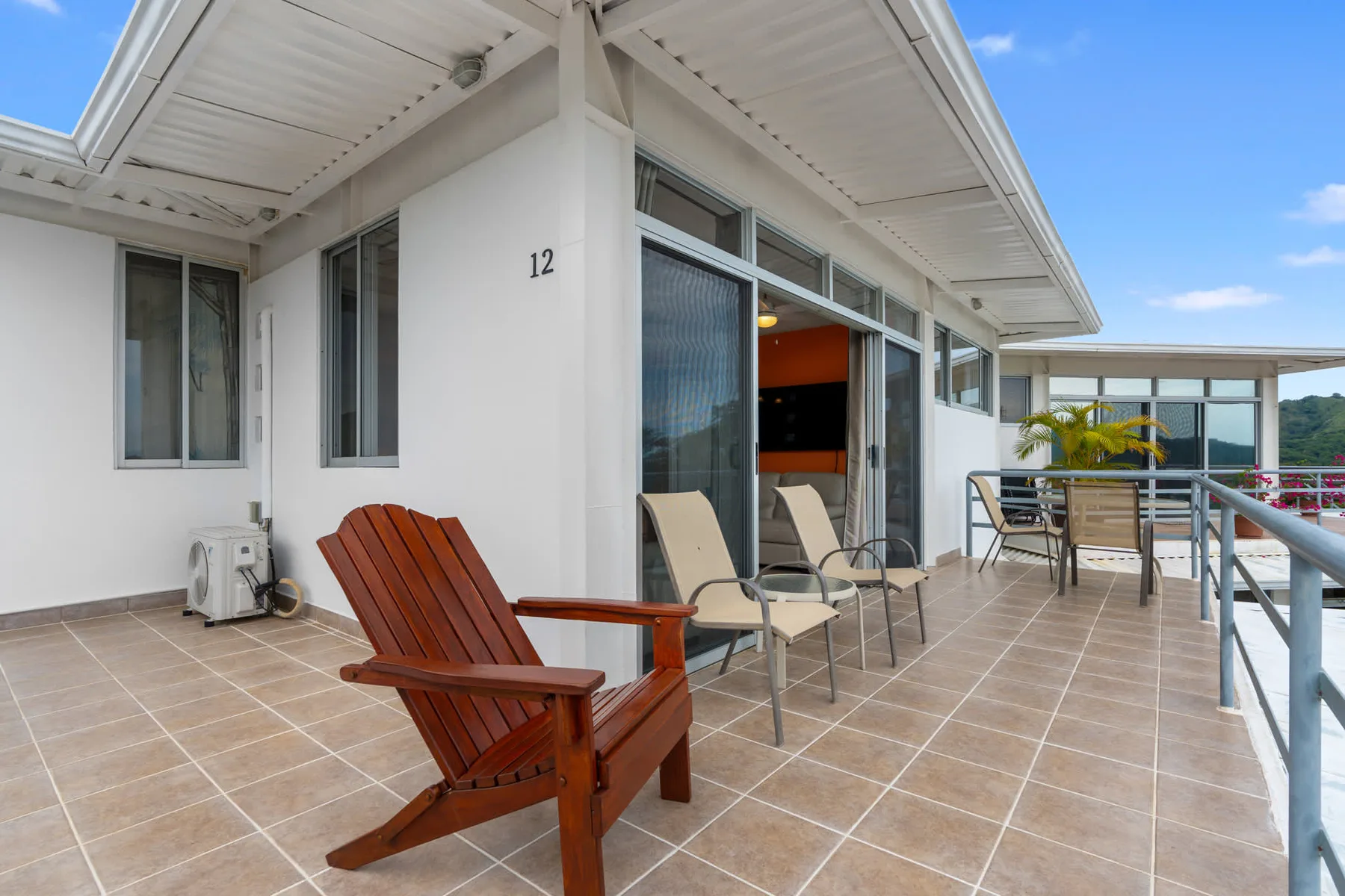 An outdoor terrace beside a white building has seating and a glass railing.