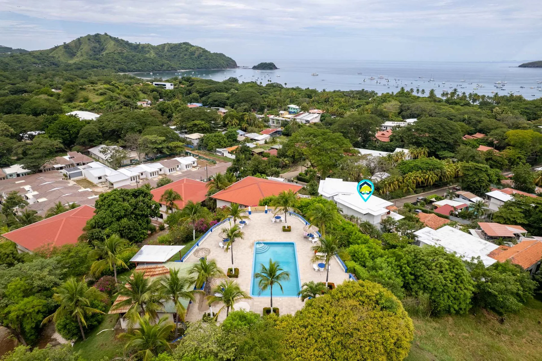 An aerial view of a coastal resort with a swimming pool, homes, and a tree-covered shoreline.