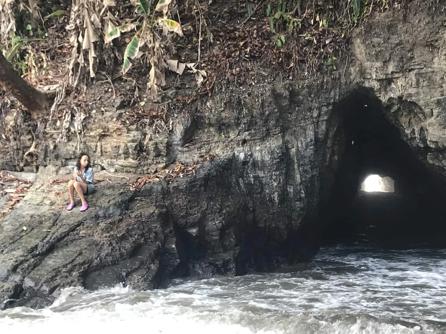 A rocky shoreline meets a dark cave opening as waves wash across the foreground.