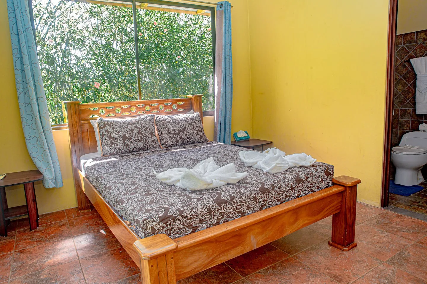 A bedroom with a wooden bed and patterned bedding beside a large window.