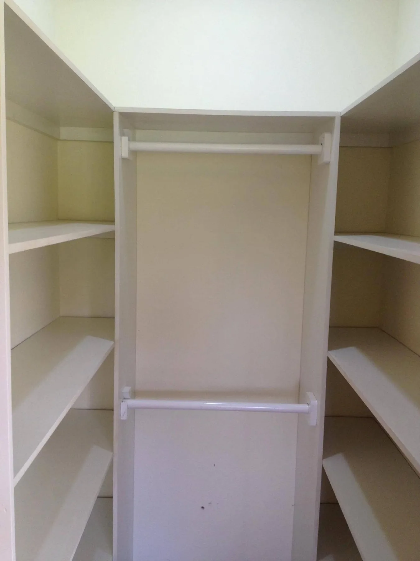 An empty built-in closet with a central hanging section and side shelves.
