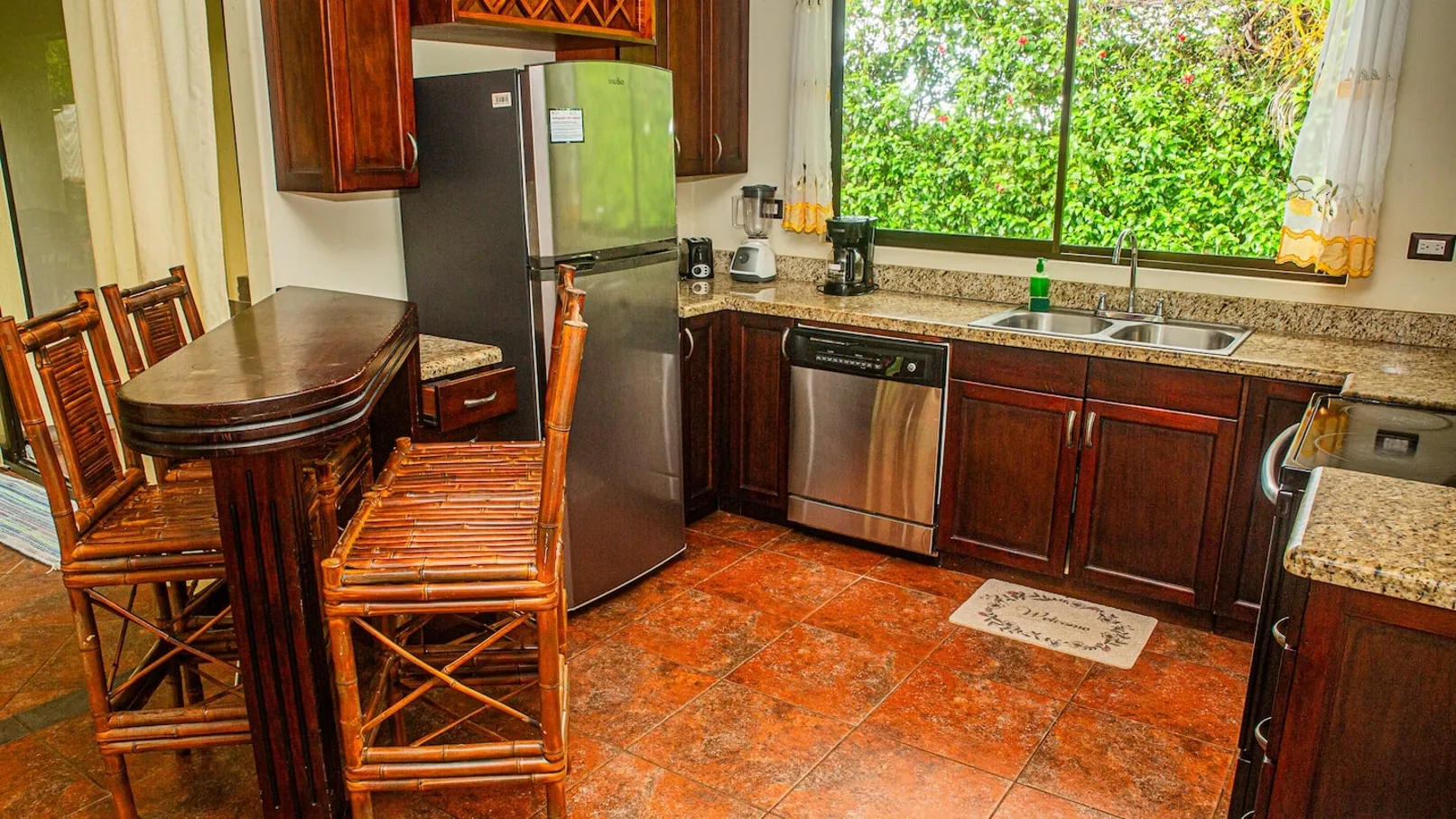 A kitchen with wooden cabinets, a refrigerator, and a sink beneath a large window.