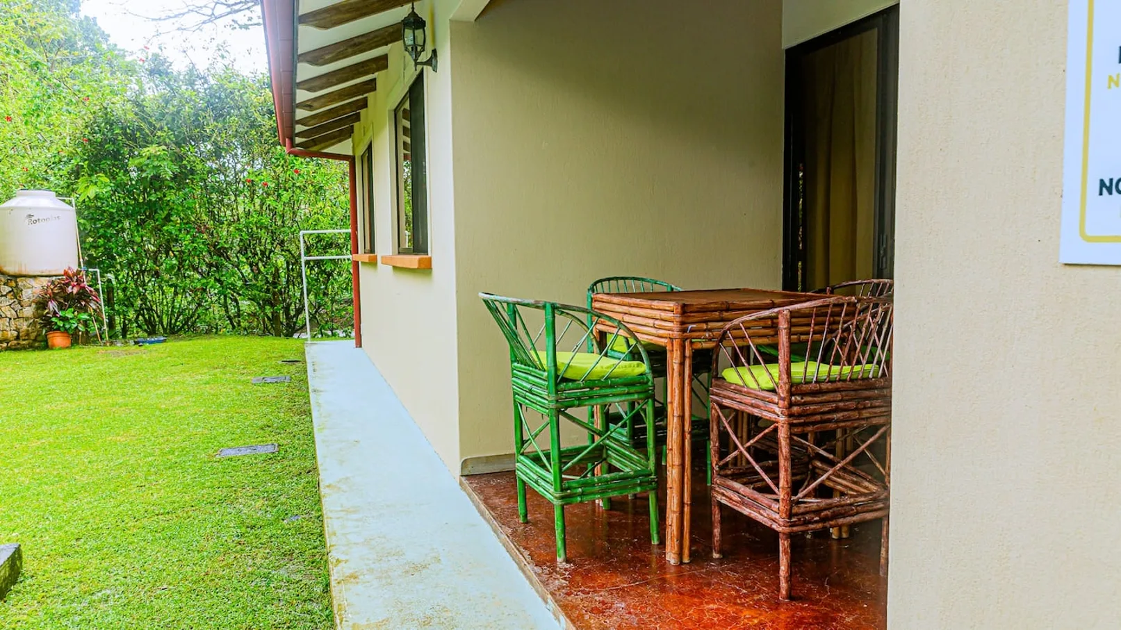 A covered patio with a small table and seating overlooks a green lawn.