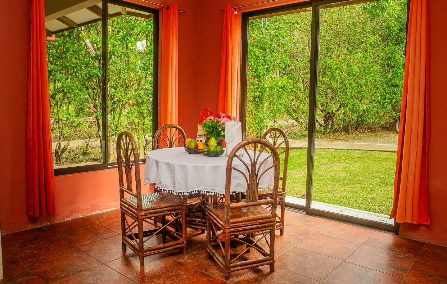 A dining table with chairs sits beside large windows overlooking a green garden.