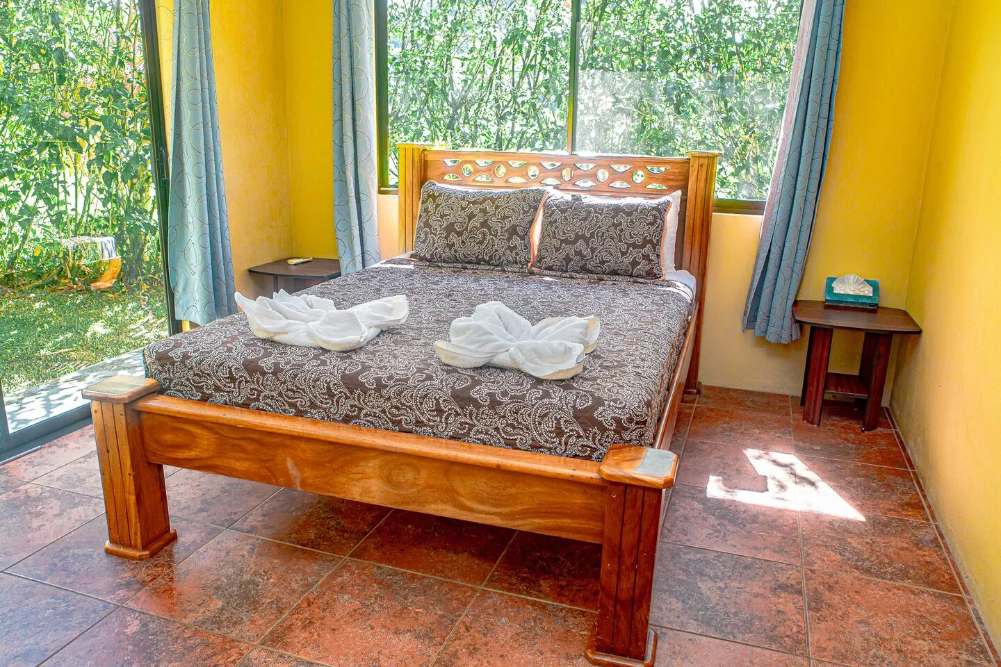 A bedroom with a wooden bed, patterned bedding, and large windows overlooking greenery.