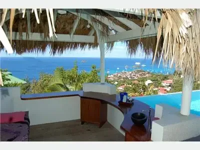 Una barra exterior techada da a una piscina, casas costeras y el mar.