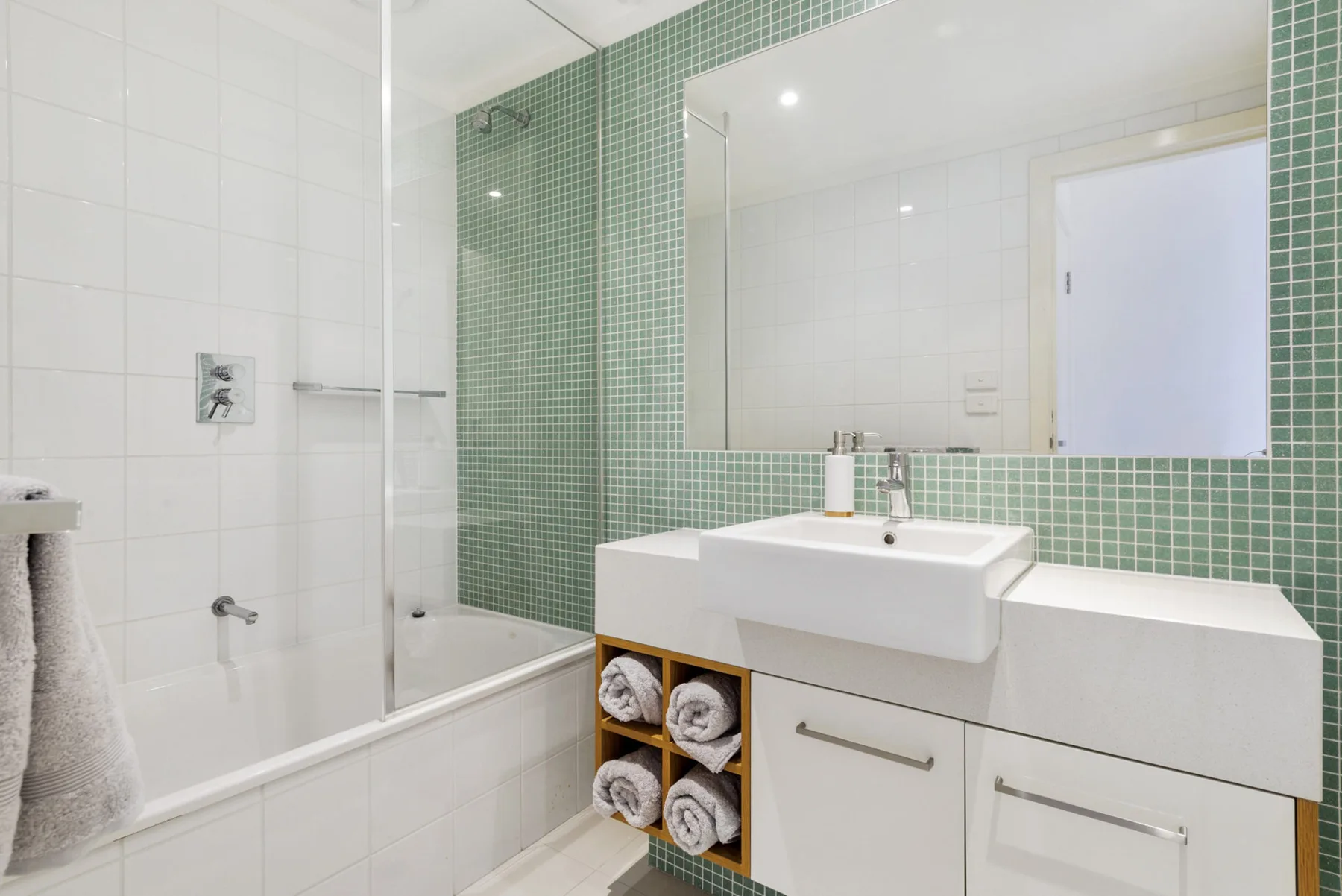 Un baño luminoso con lavabo, espejo y ducha de cristal.