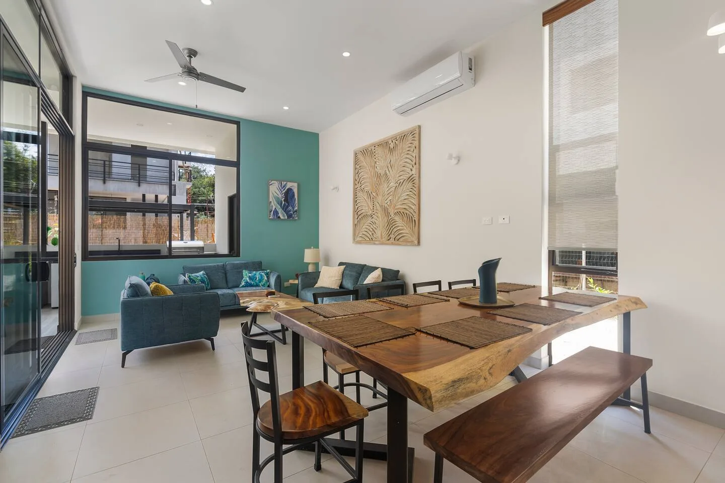 A bright living and dining area with a teal seating nook and wooden dining table.