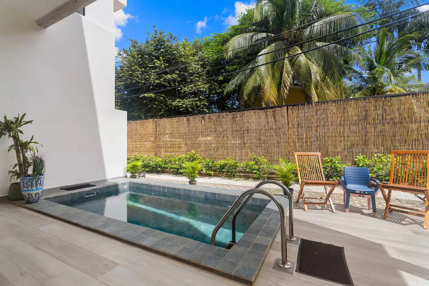 A small outdoor pool sits beside a deck with seating and tropical plants.