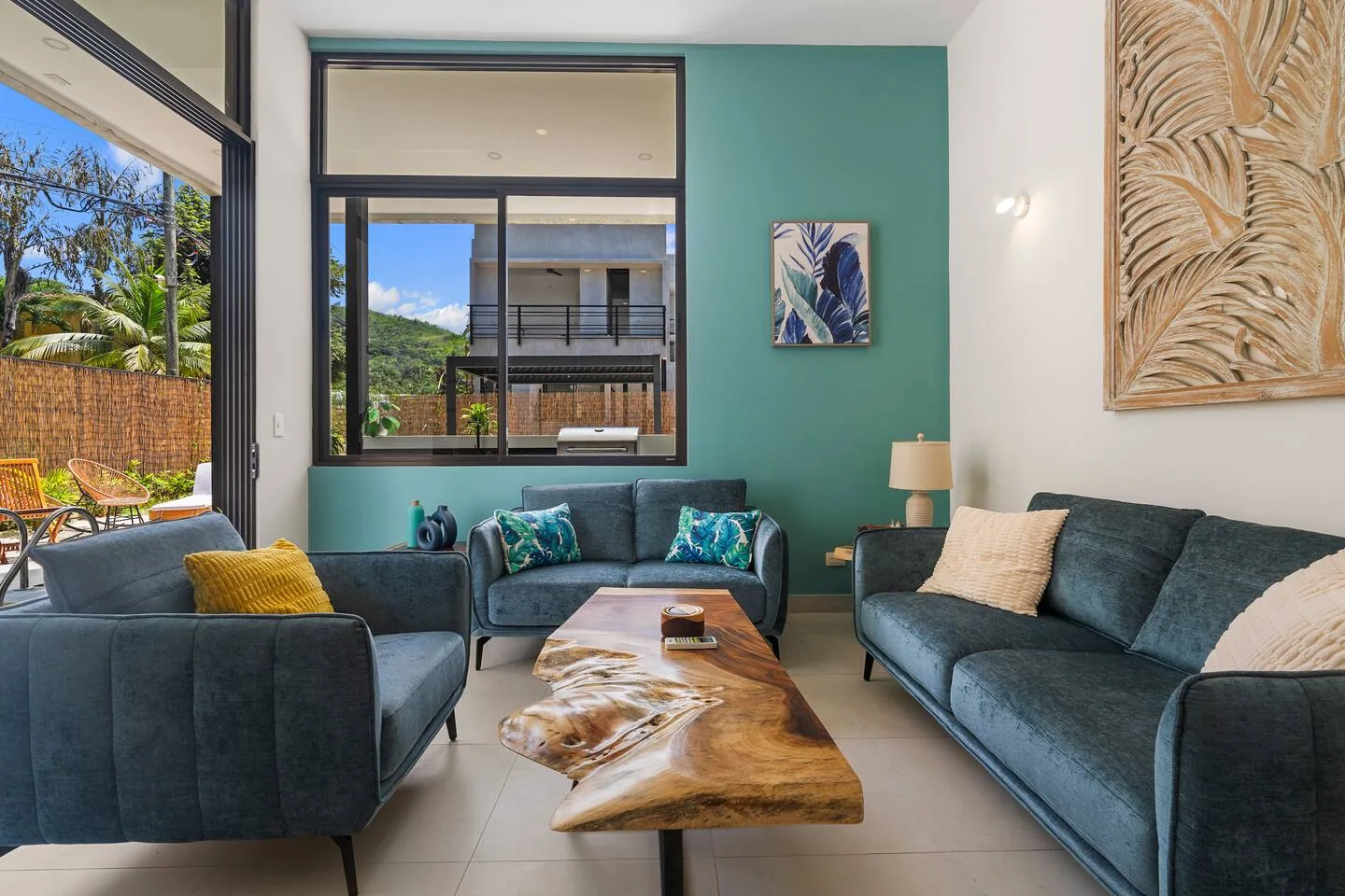 A living room with blue seating around a wooden coffee table and large windows.