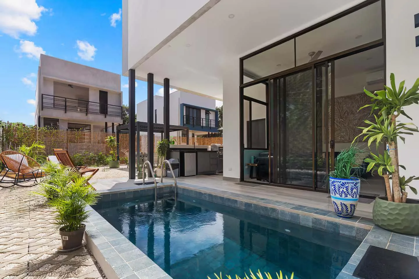 A modern home opens onto a small swimming pool and outdoor seating area.