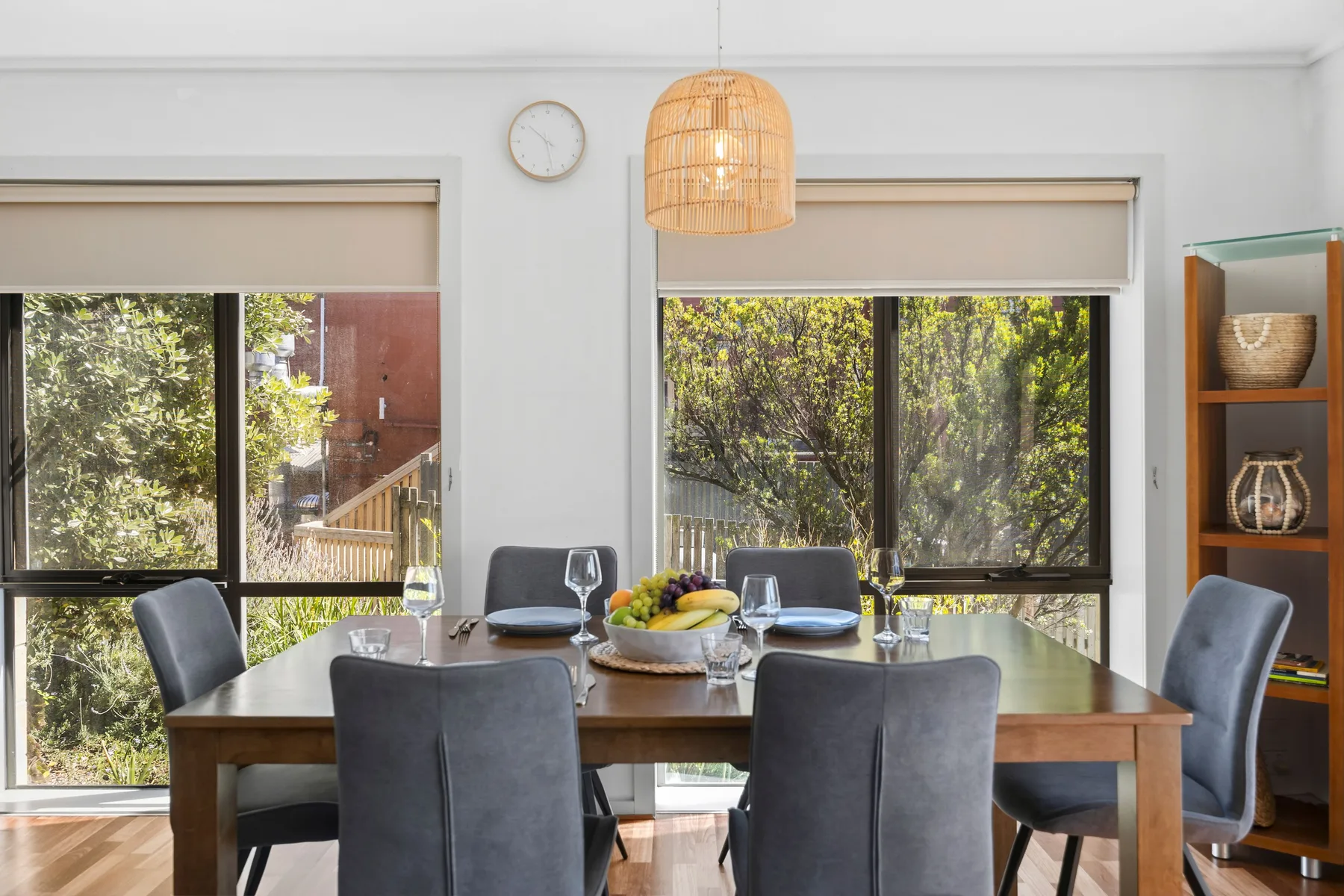 Un comedor con una mesa de madera, asientos grises y grandes ventanas.