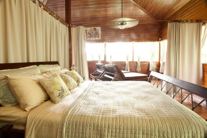 A bedroom with a large bed and a sitting area beside bright windows.