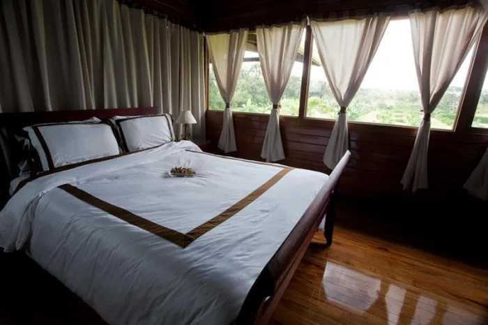 A bedroom with a neatly made bed beside curtained windows.