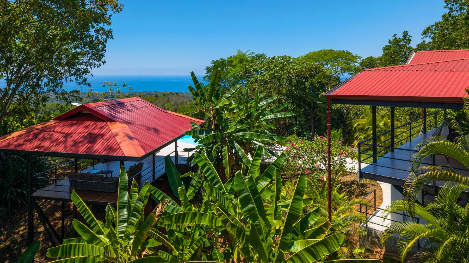 A tropical property with red-roofed buildings amid lush greenery and a distant ocean view.
