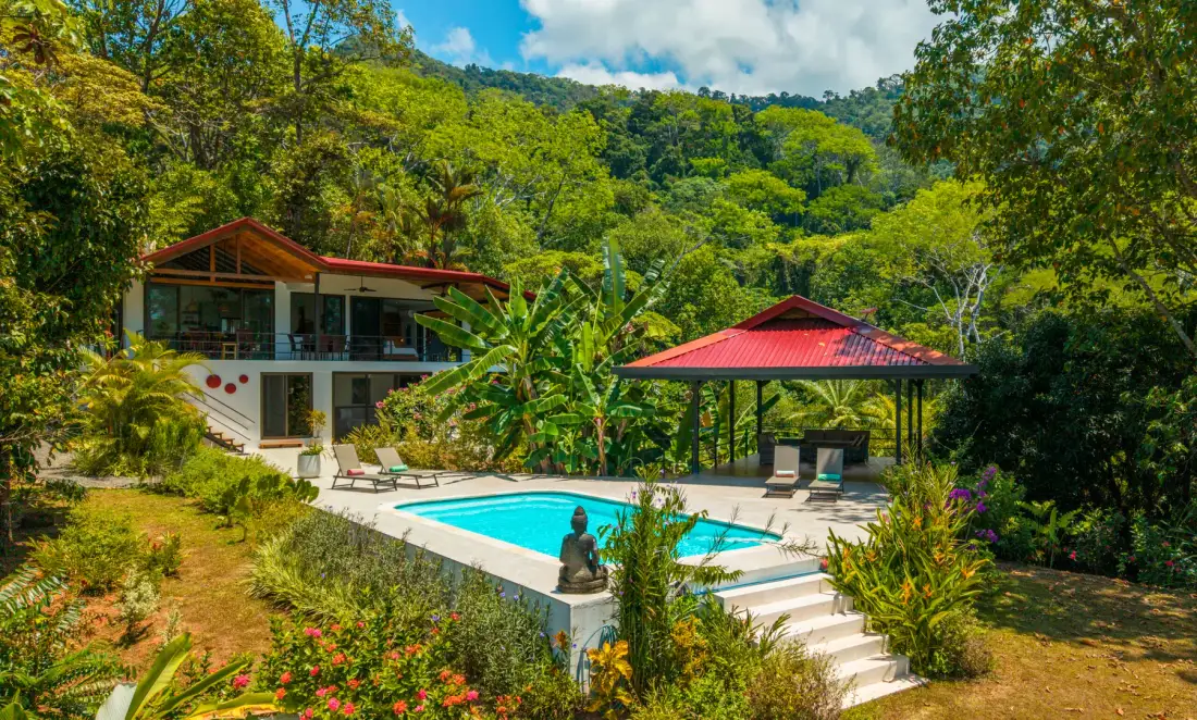A hillside property with a swimming pool, a house, and a red-roofed pavilion.
