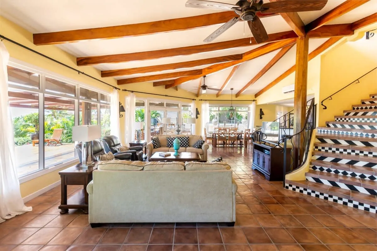 A spacious living room with seating, large windows, and exposed ceiling beams.