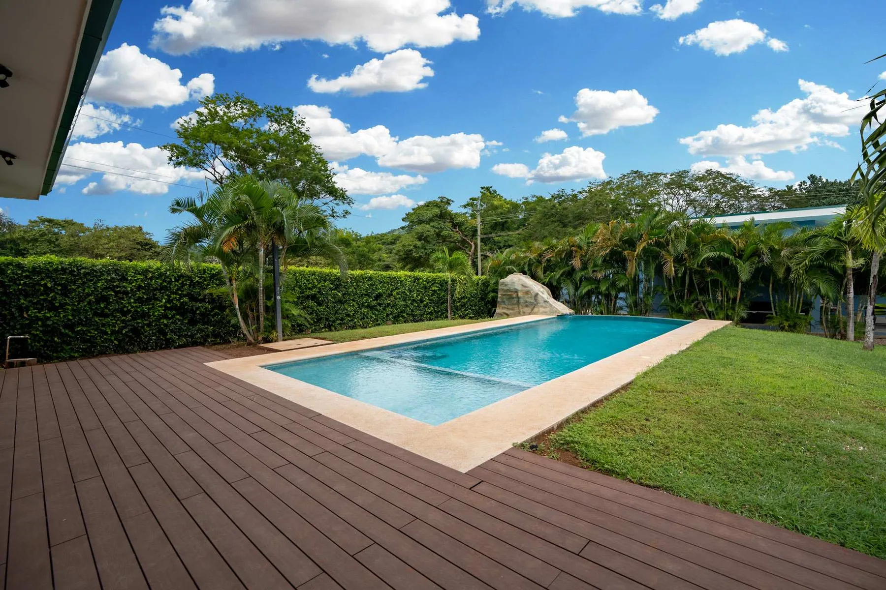 An outdoor swimming pool sits beside a wooden deck and green lawn.