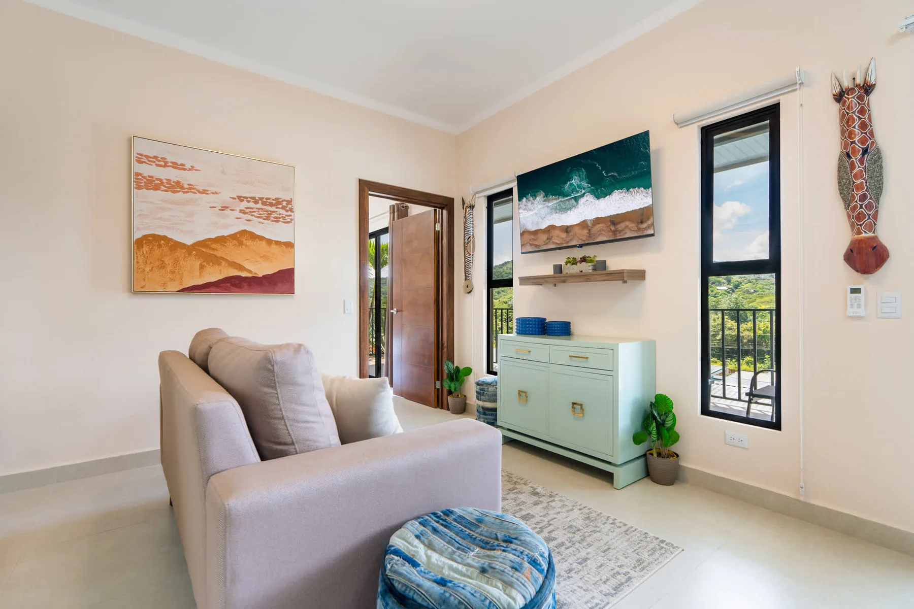 A bright living room with seating, framed artwork, and a tall window.