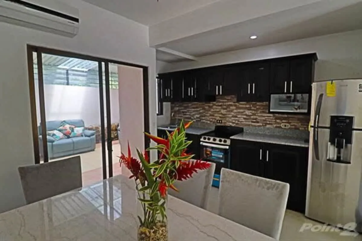 A dining area and kitchen with a table, dark cabinets, and a refrigerator.
