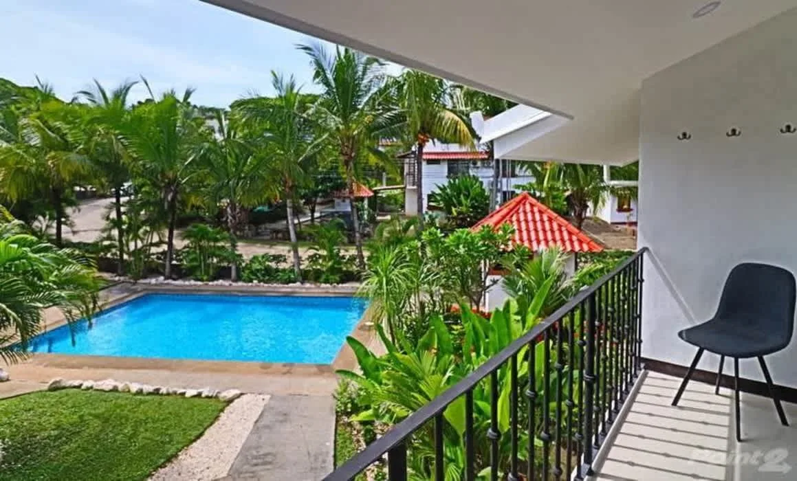 A covered balcony overlooks a swimming pool surrounded by tropical plants.