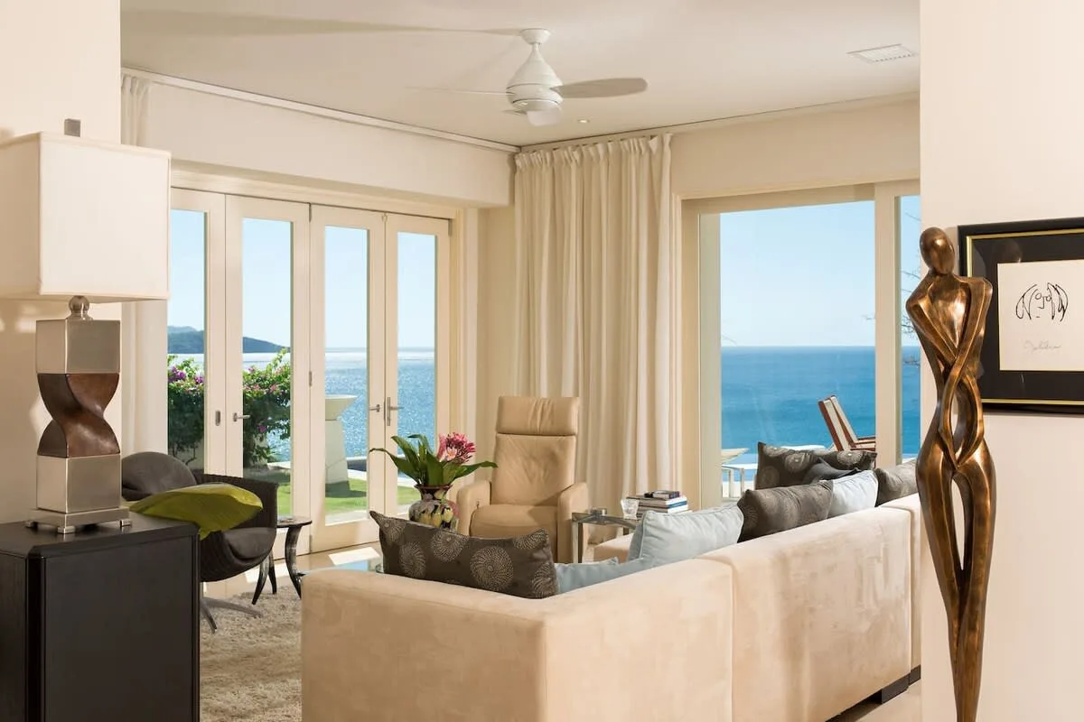 A bright living room with seating, large windows, and views of the ocean.