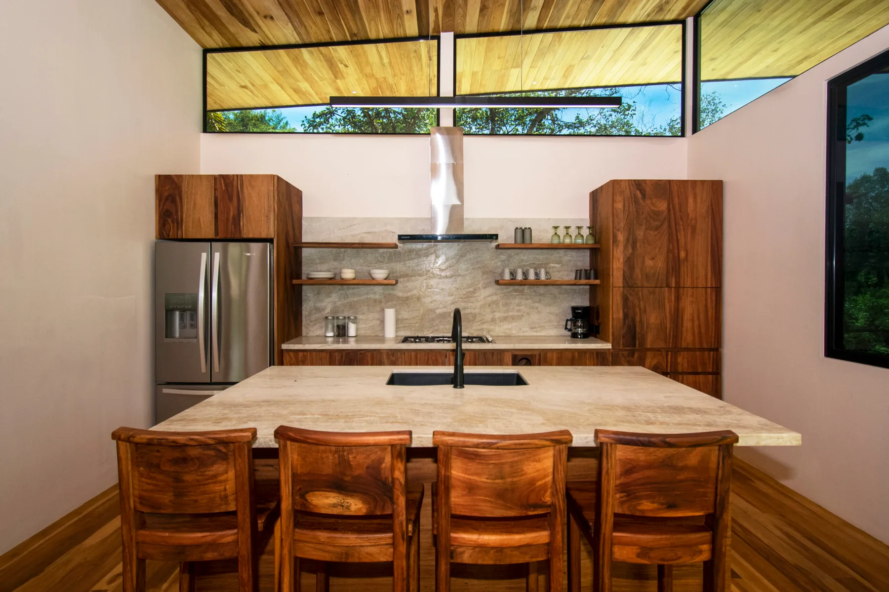 A kitchen with a broad island and wooden seating beneath a wood-paneled ceiling.