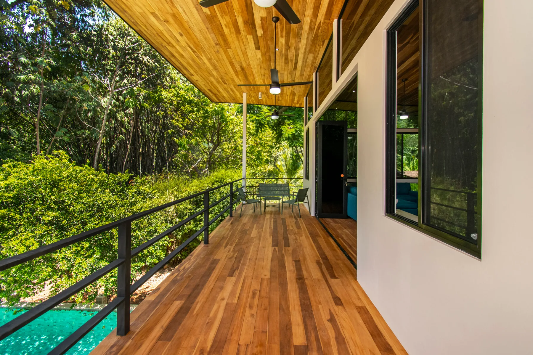 A covered wooden deck runs beside the house, overlooking leafy trees.