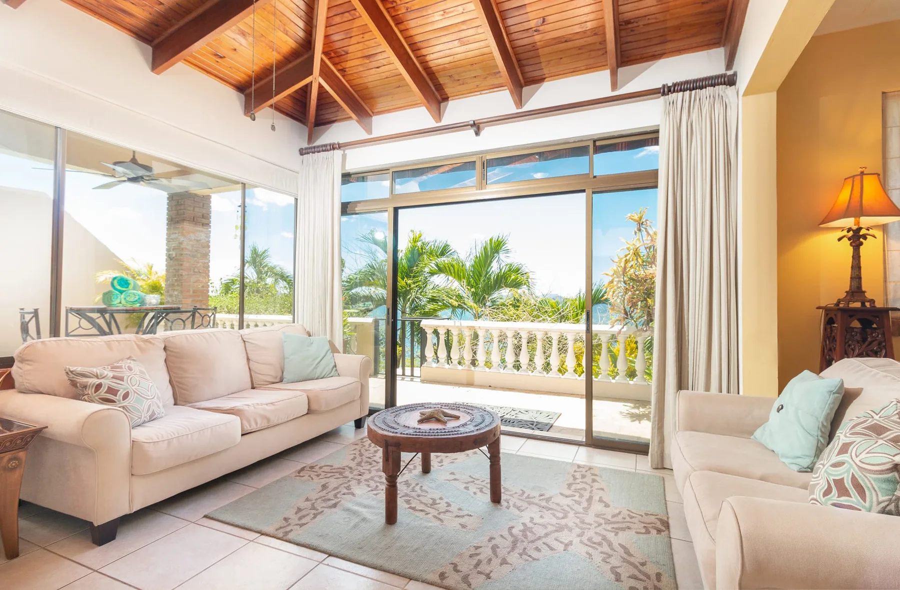 A bright living room with seating around a coffee table and glass doors opening to a balcony.