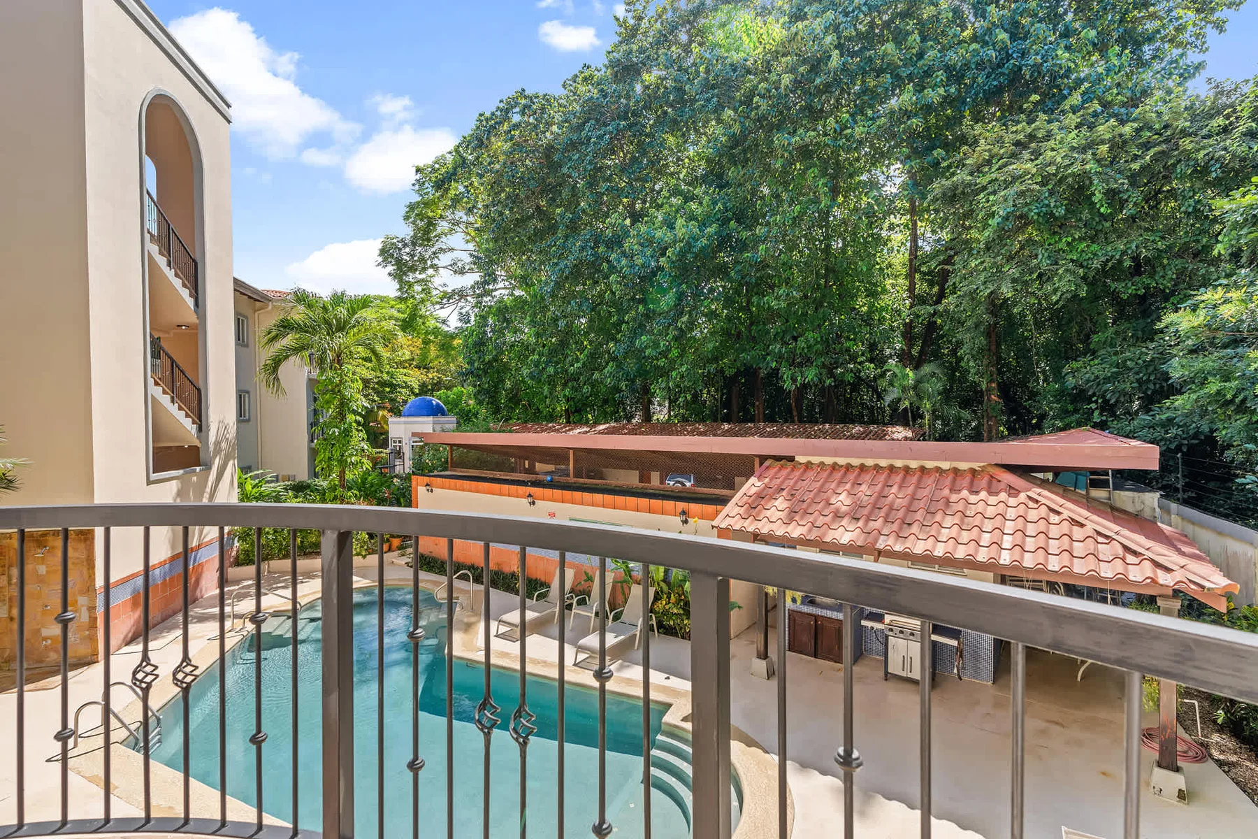 A swimming pool beside a building, viewed over a metal railing.