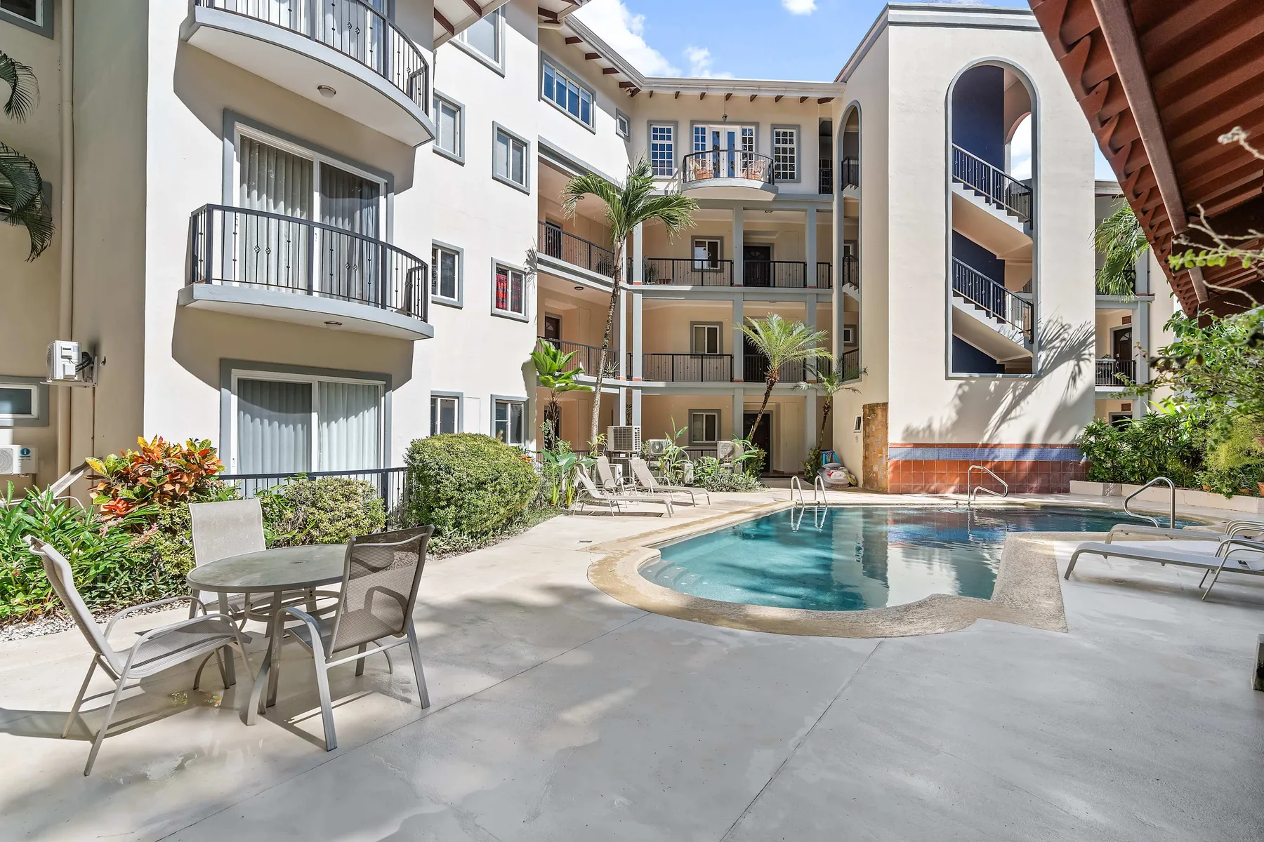 An apartment courtyard with a swimming pool, surrounding balconies, and patio seating.