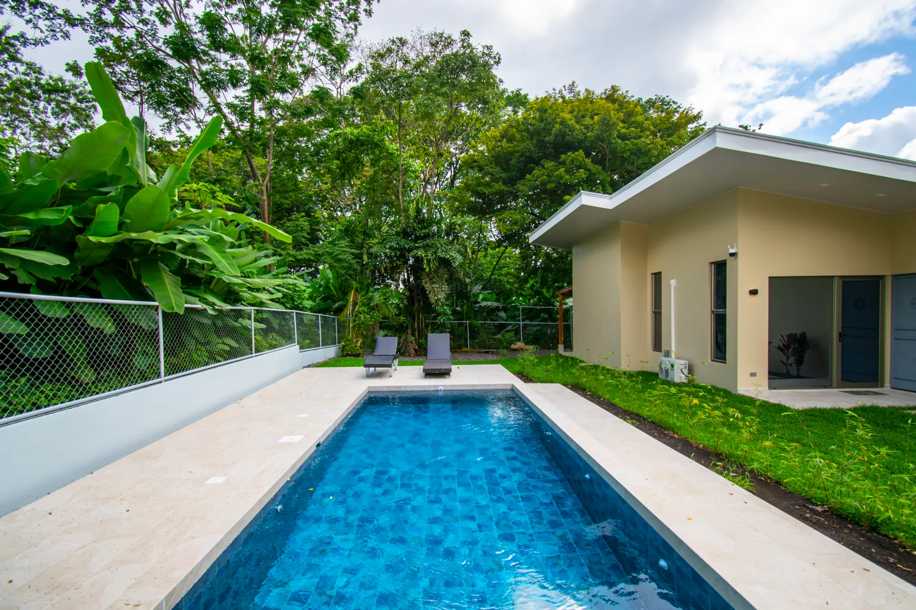 Una piscina exterior junto a un edificio moderno bajo, rodeada de vegetación.
