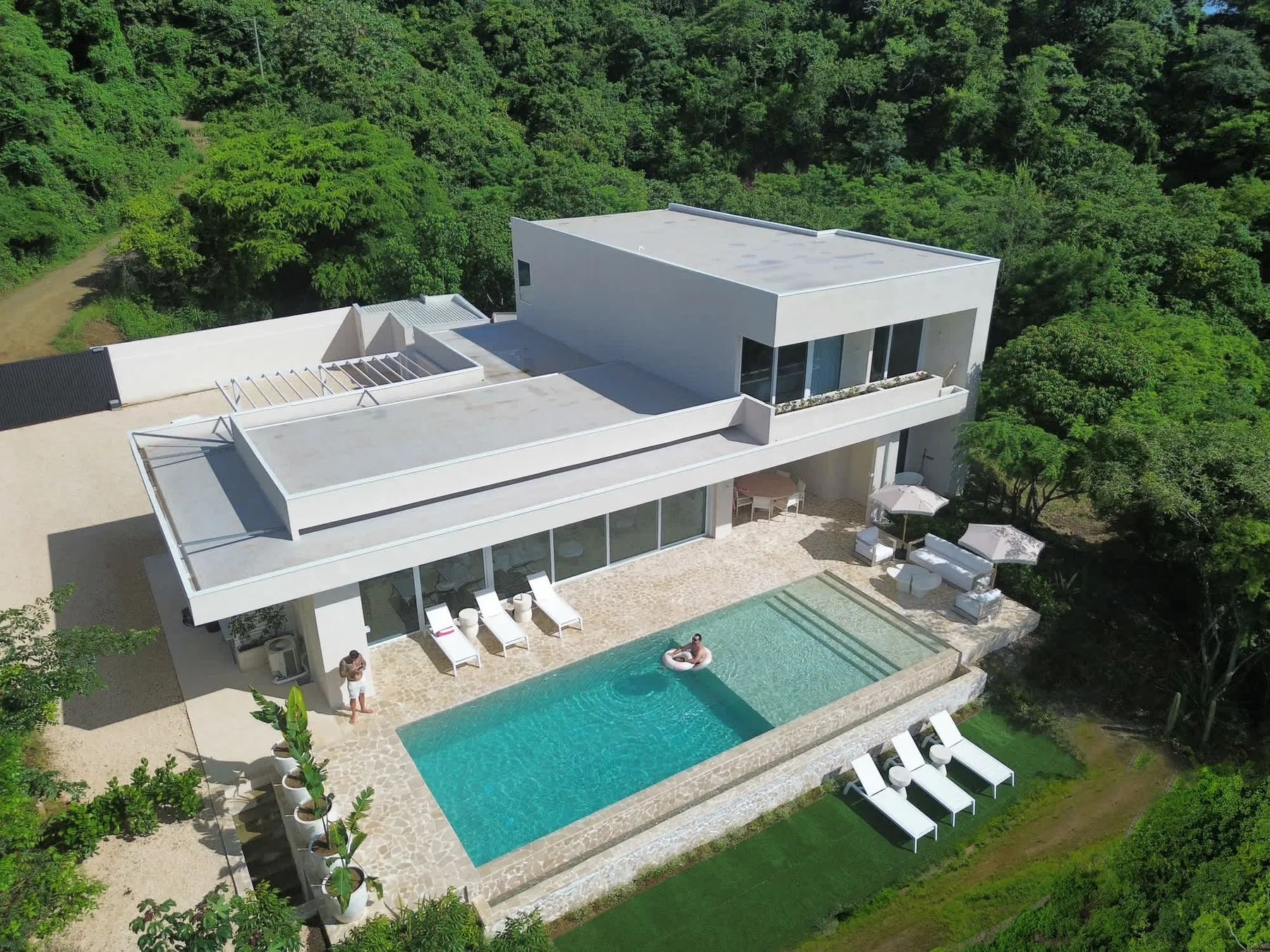 A modern house with a swimming pool and lounge seating, surrounded by greenery.