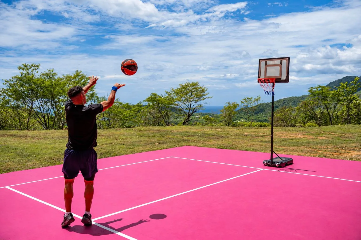 A person shoots a basketball on a bright pink outdoor court.