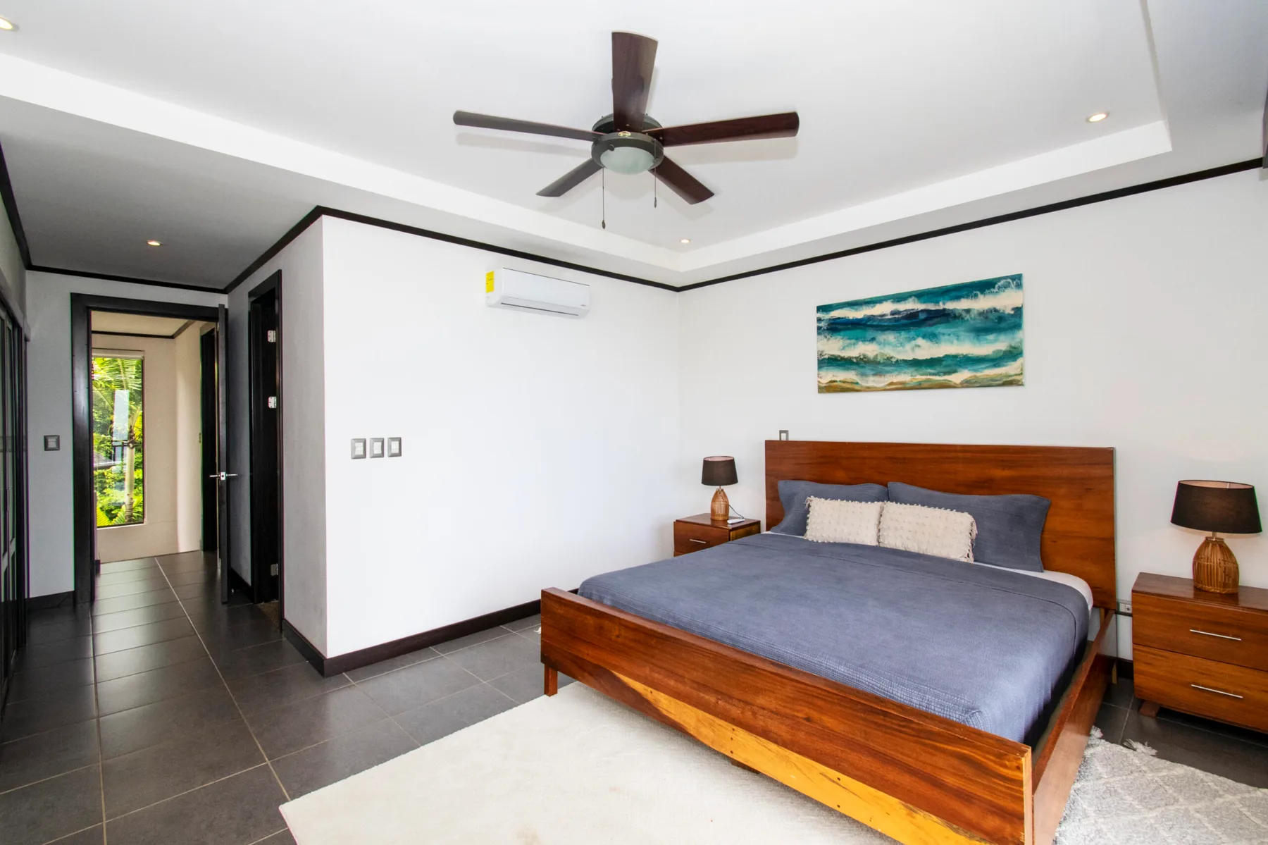 Un dormitorio con una cama de madera, ropa de cama azul y un cuadro sobre el cabecero.