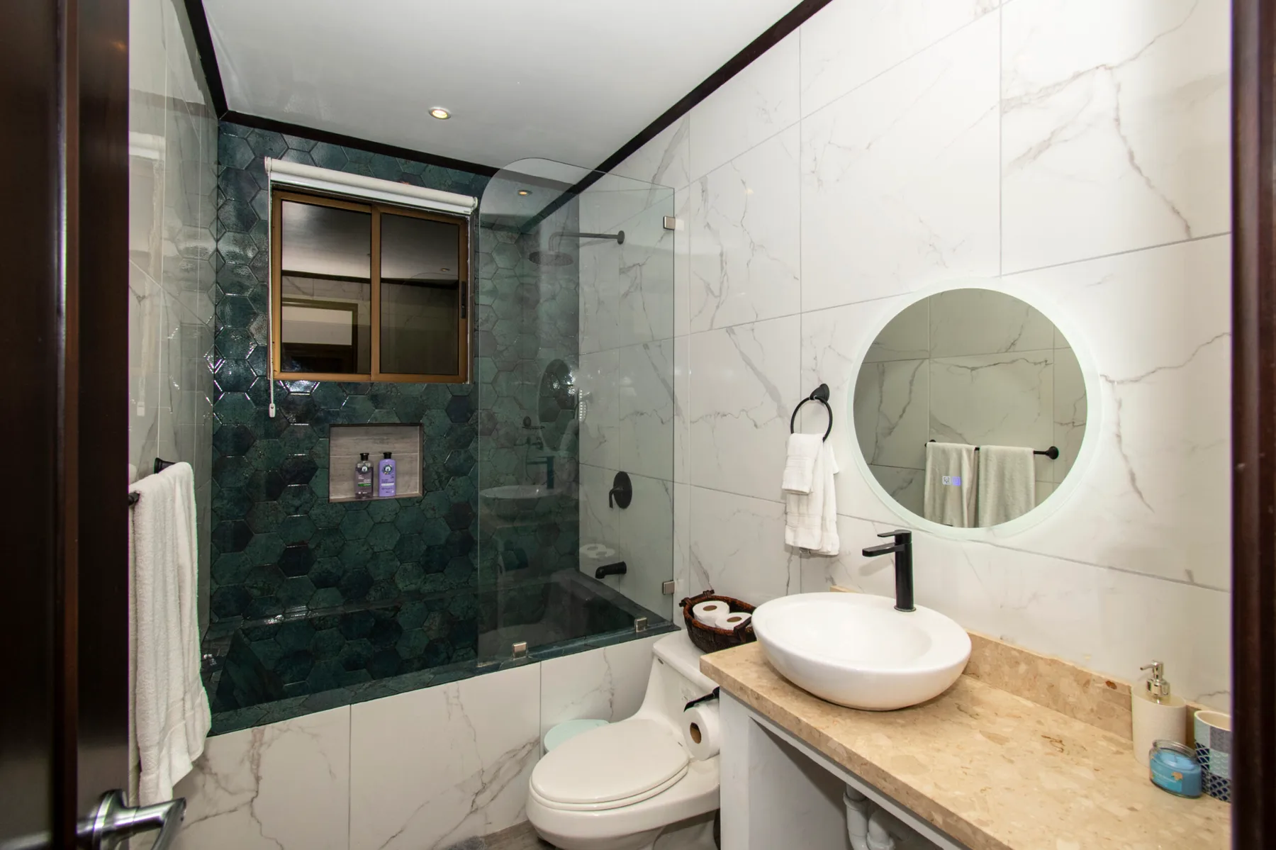 Un baño revestido de mármol con ducha de vidrio, inodoro y lavabo.