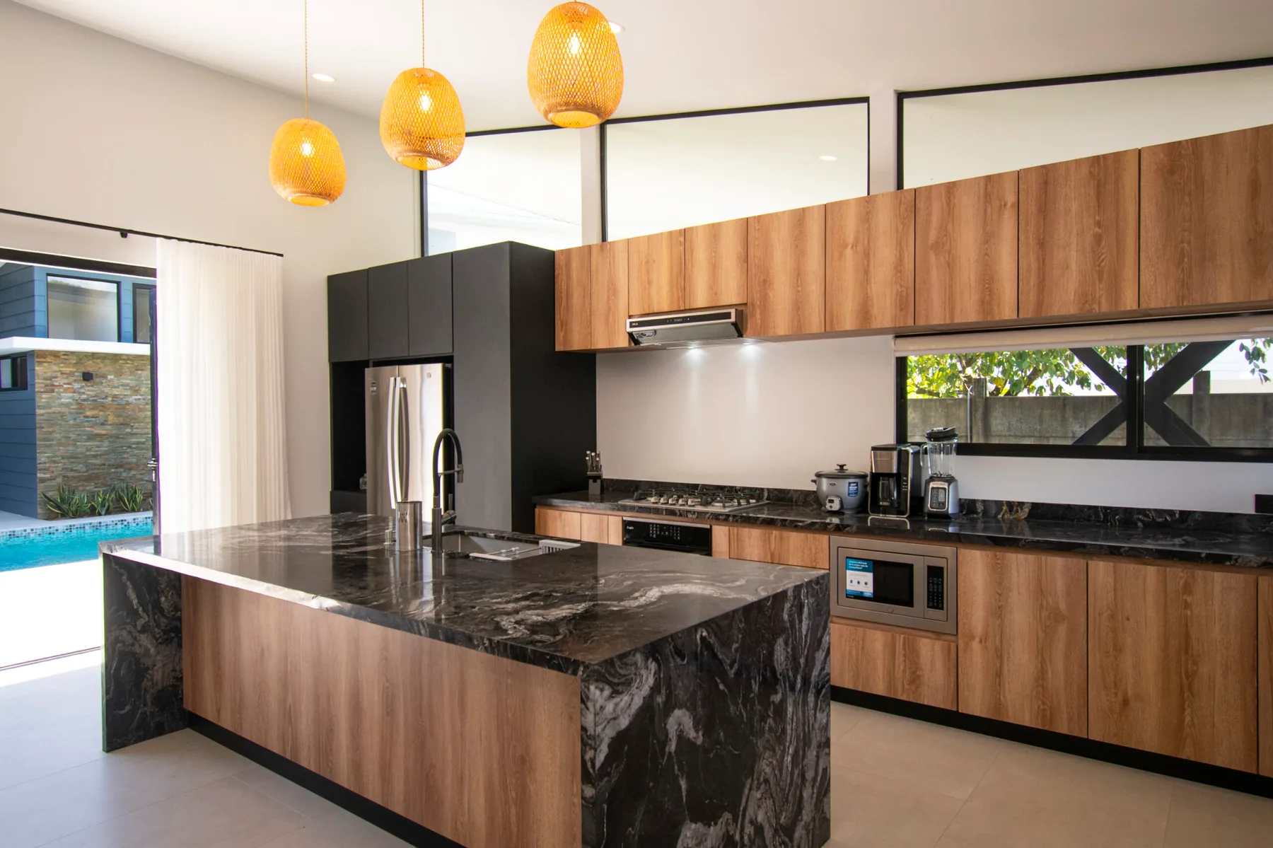A modern kitchen with wood cabinetry, dark countertops, and a large island.