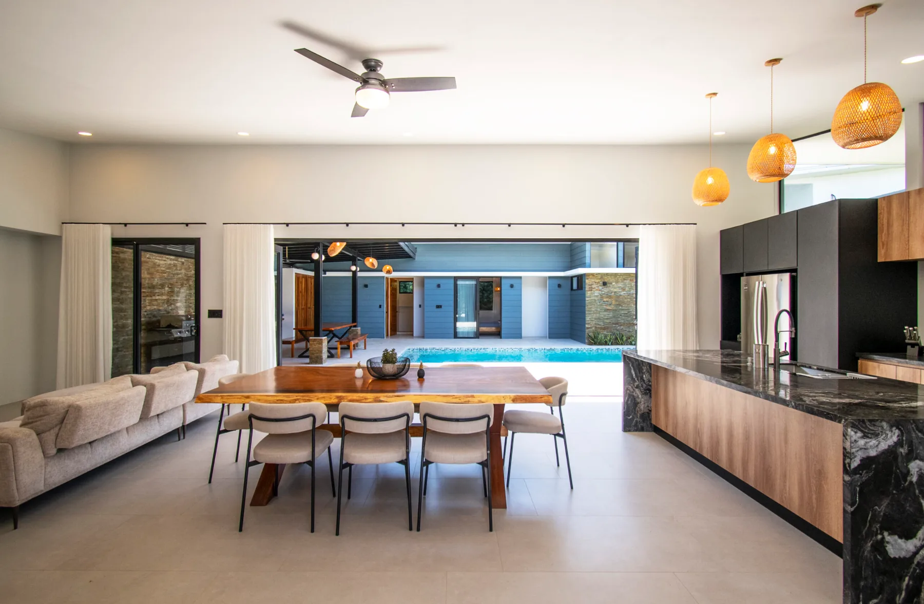 An open-plan kitchen and dining area overlooks a swimming pool through wide glass doors.