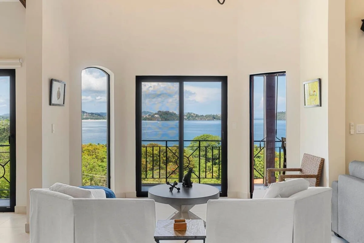 A bright living room opens onto a balcony overlooking the water.
