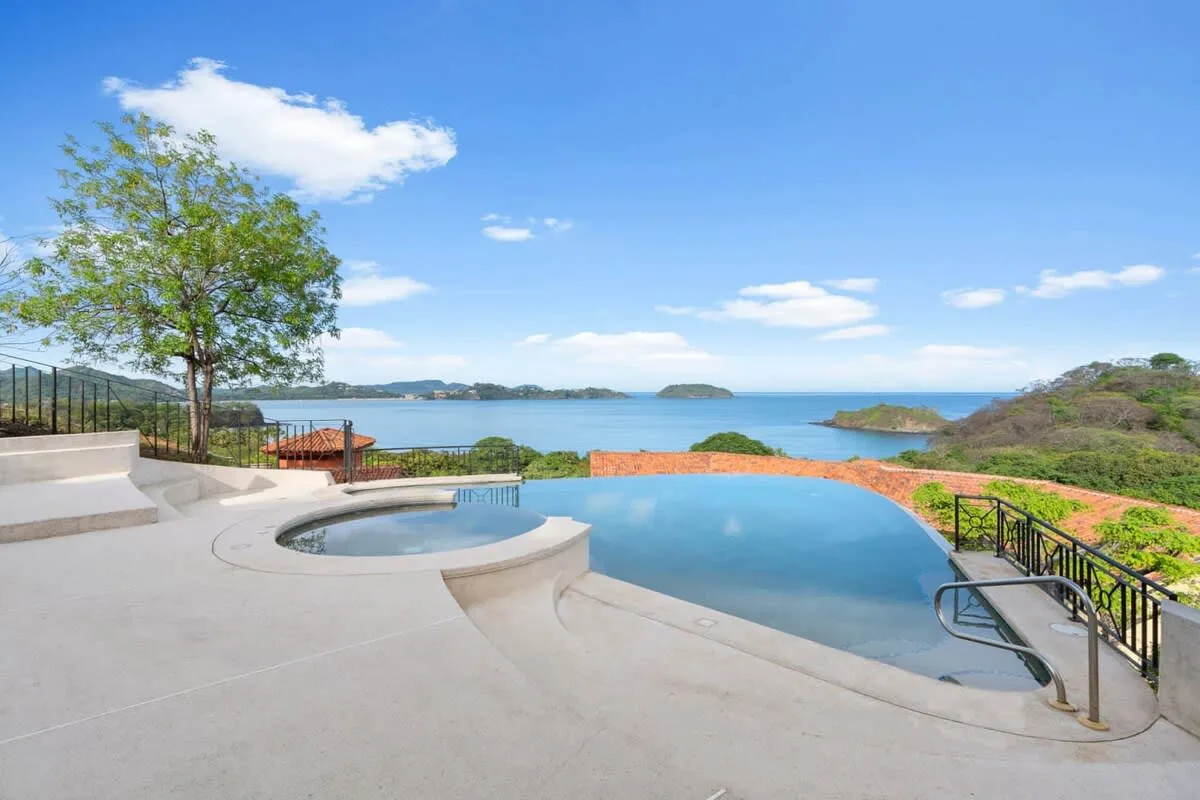 An outdoor pool and circular spa overlook the ocean from a paved terrace.