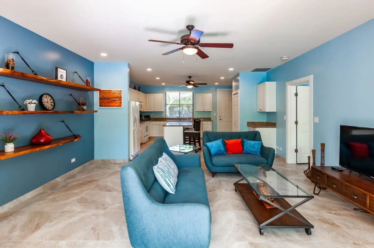 Una sala azul con asientos, una mesa de centro de vidrio y una cocina abierta.