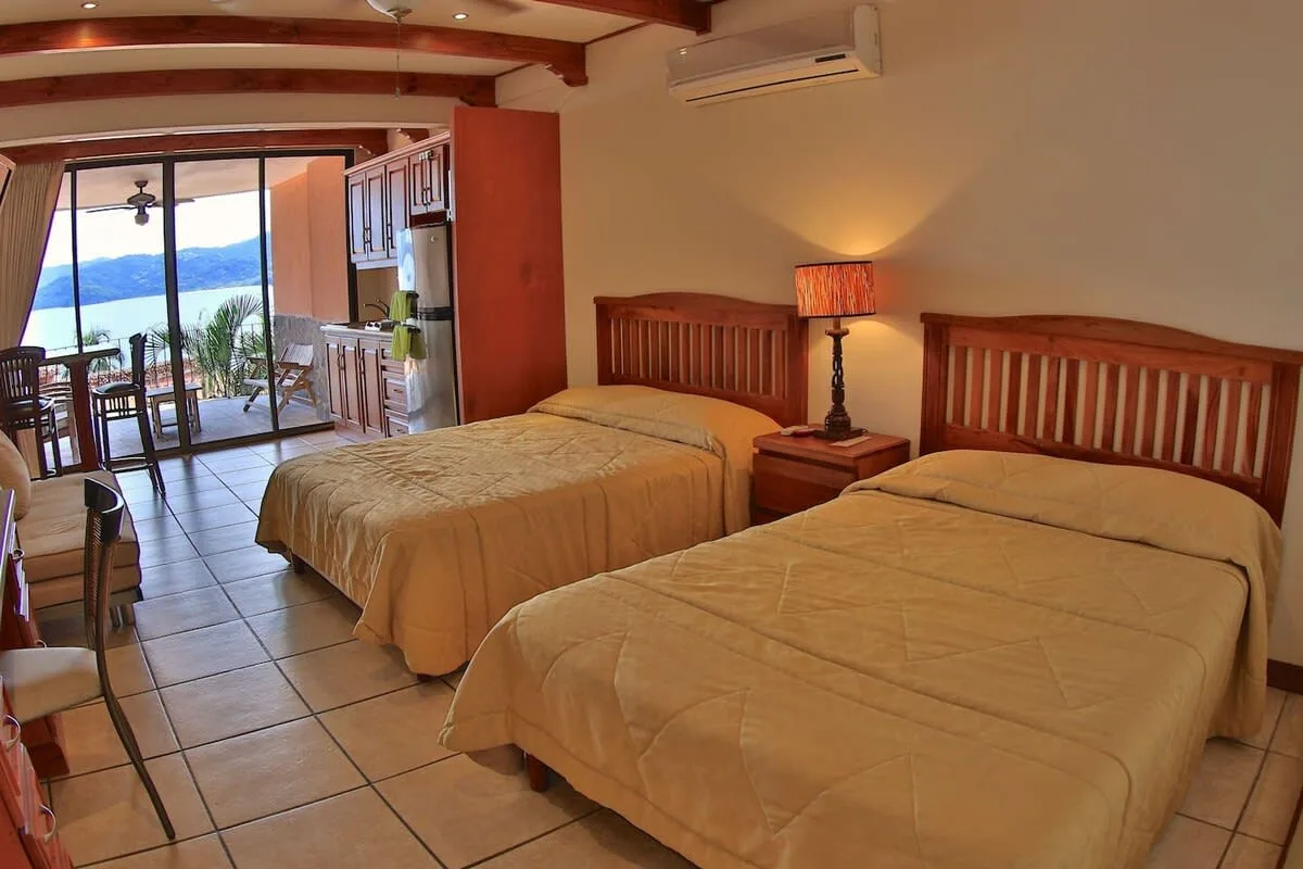 A bedroom with two beds and a sliding glass door opening to a balcony.