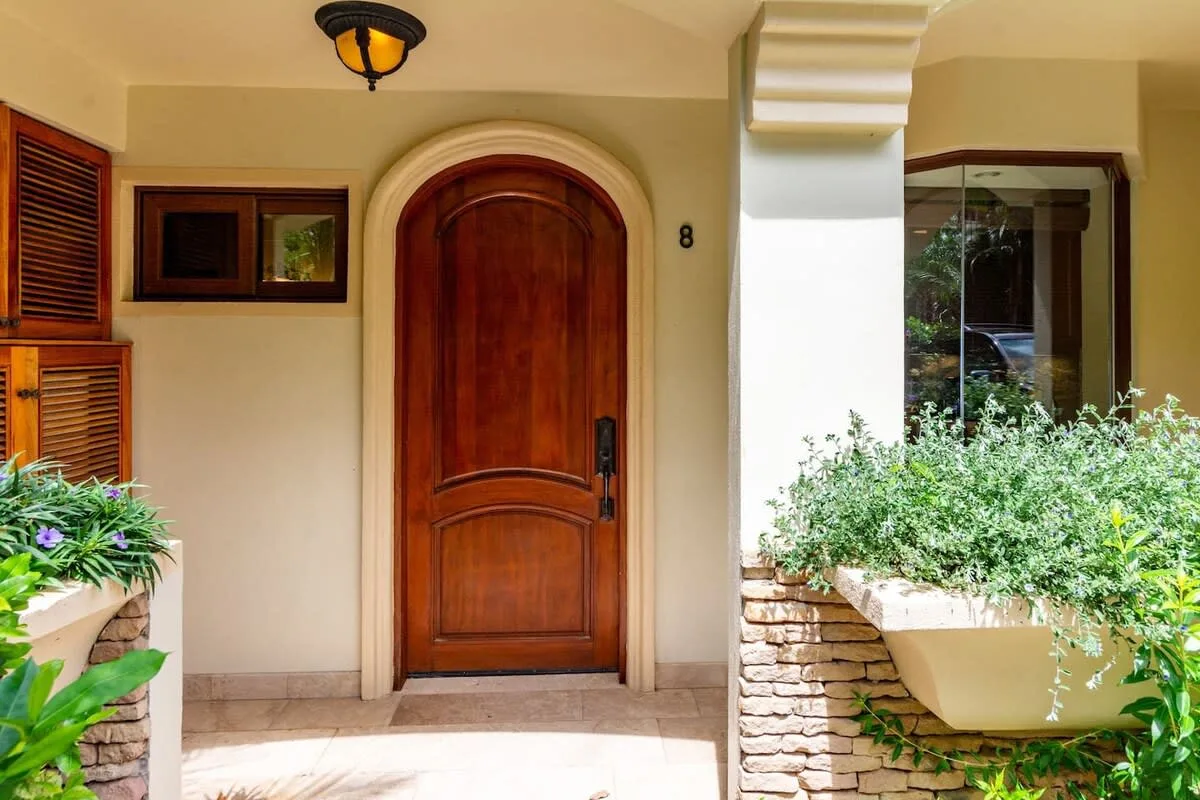 A home entrance with an arched wooden door and leafy planters.