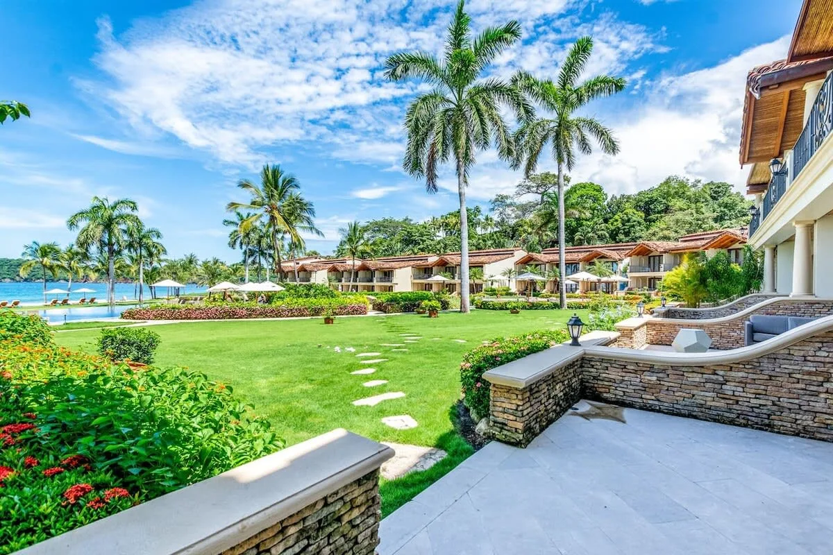 A landscaped resort garden with palm trees, a paved patio, and ocean views.
