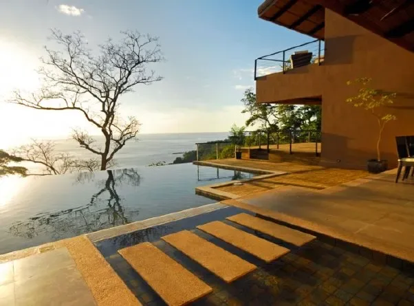 An outdoor pool and terrace beside a modern building overlook the water.