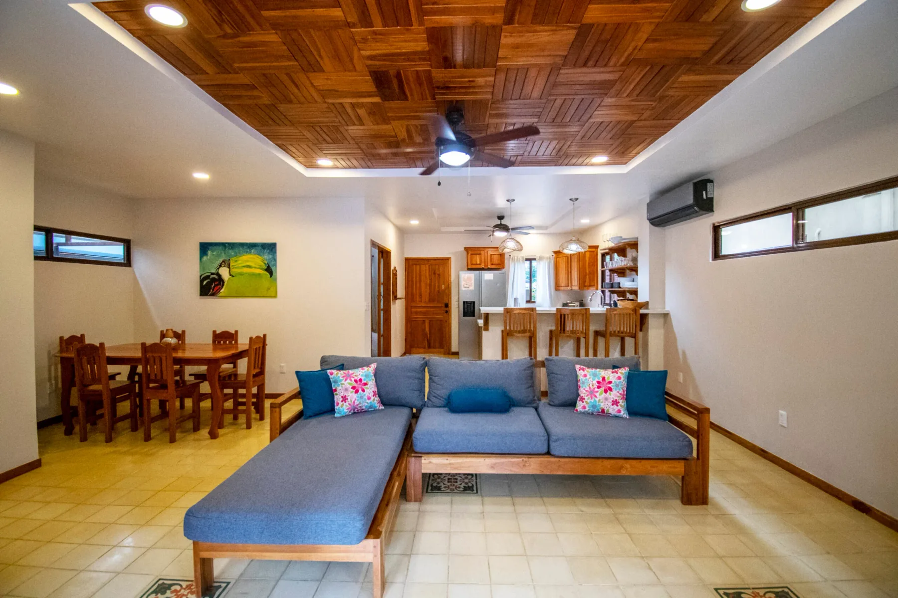 A living room with an L-shaped sofa and a dining area behind it.