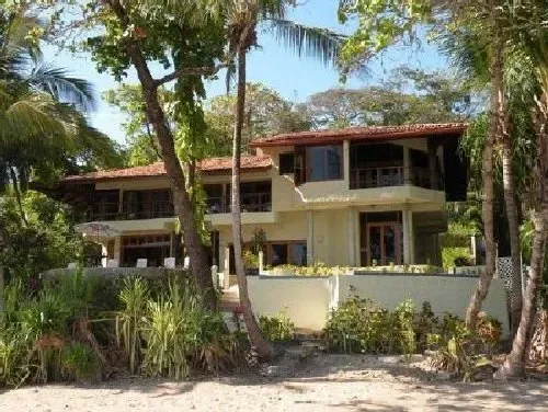 A multi-level house stands among trees and tropical plants.