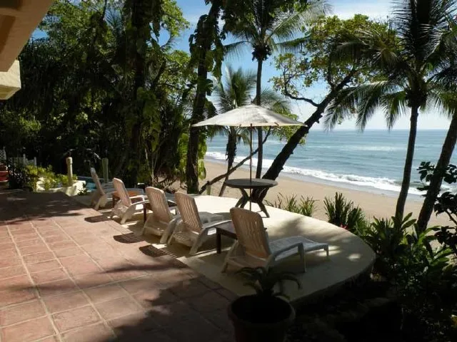 A seaside patio with lounge seating and an umbrella overlooks the beach and ocean.